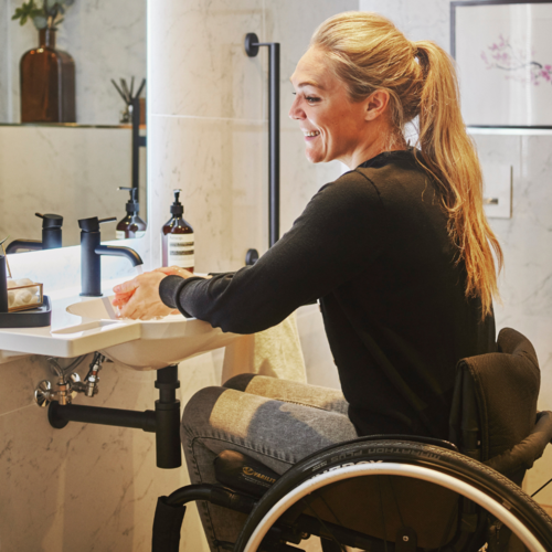 Sophie Morgan washing hads at basin in her new Fine & Able bathroom seated in a wheelchair
