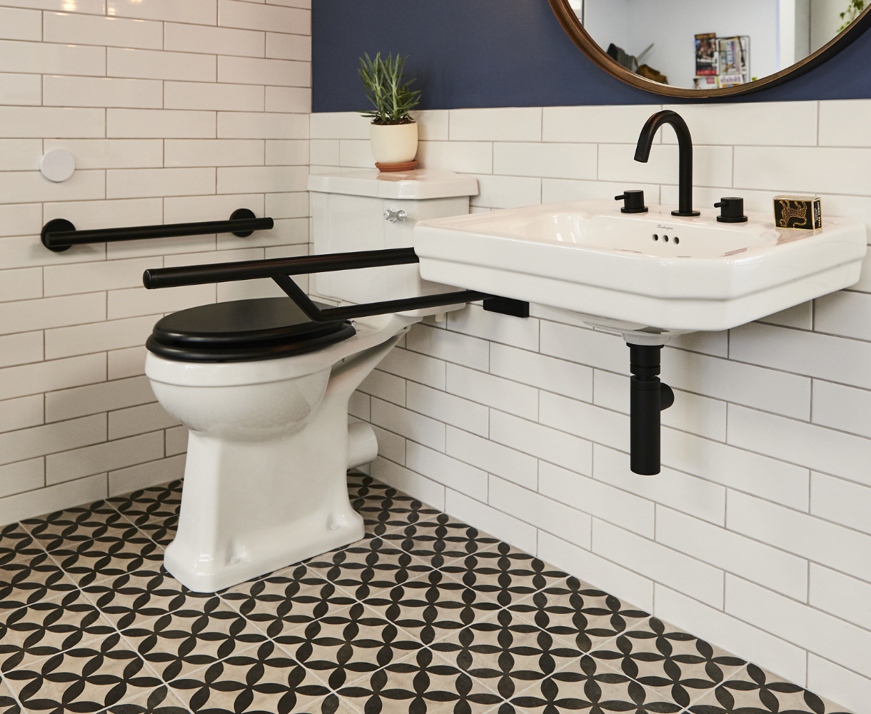 Comfort height toilet and basin in a traditional style with matt black grab rails and taps. Monochrome pattern tiled floor and white metro tiles