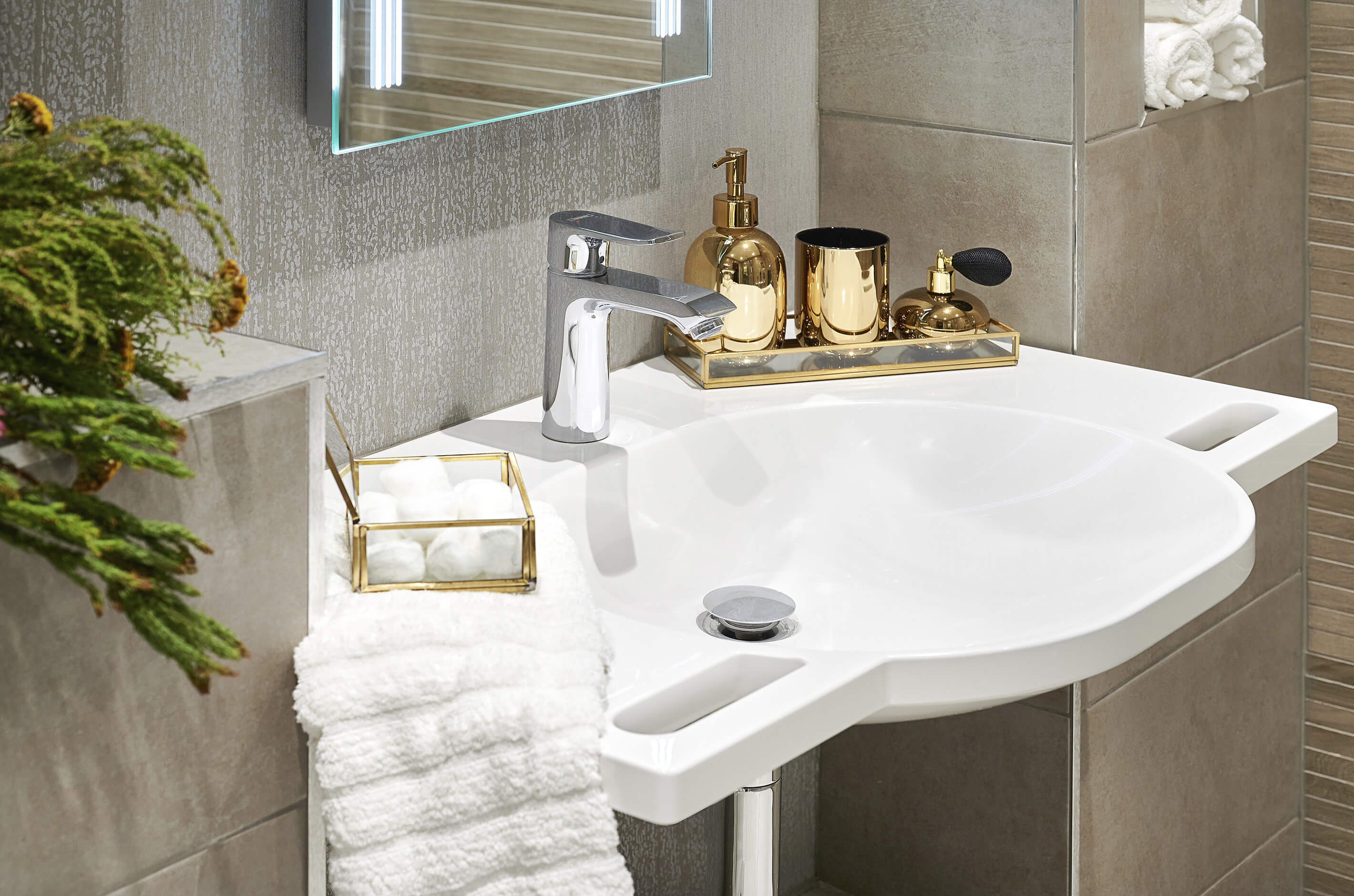 Basin with integrated hand grips with mirror above, with gold accessories and white hand towel in grips.